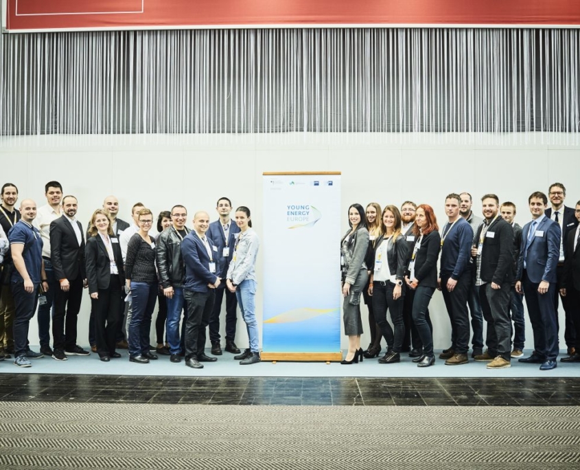 Gruppenfoto von etwa 30 Personen auf einer Bühne. In der Mitte steht ein Roll-up von Young Energy Europe.