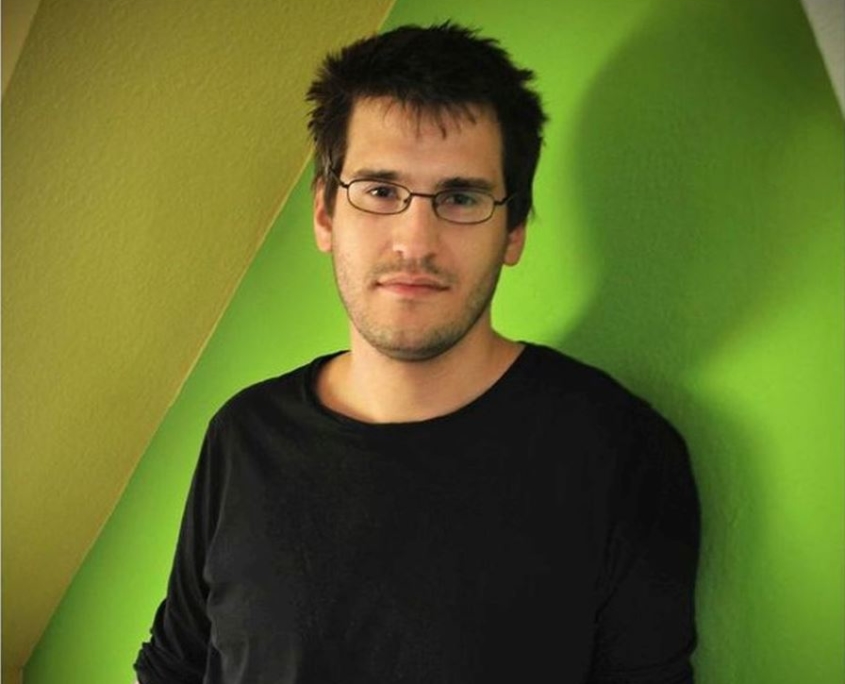 Portraitfoto von einem jungen Mann mit Brille und einem dunklen Pullover.
